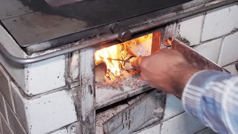 Man-uses-a-poker-to-level-wood-and-a-hearth-in-a-rustic-old-kitchen-stove