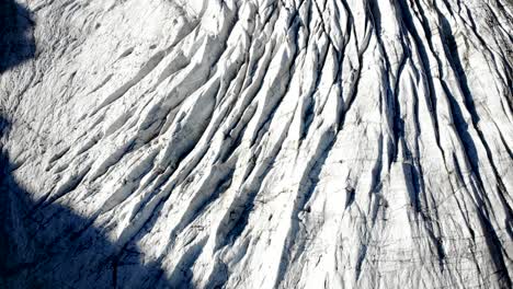 Aerial-flyover-over-the-the-crevasses-of-Morteratsch-glacier-in-Engadin,-Switzerland-at-dawn-with-an-overhead-birdseye-view-of-the-ice
