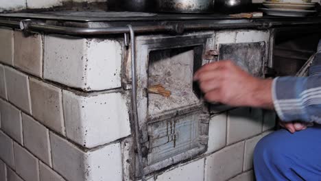 Man-opens-door-and-puts-wood-in-a-rustic-old-kitchen-stove