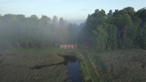 Red-Swedish-Lake-hut-in-misty-forest,-drone-pull-back-shot