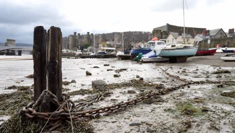 Rusting-chains-and-rotten-old-pier-wood-debris-on-Conwy-castle-harbour-riverbank