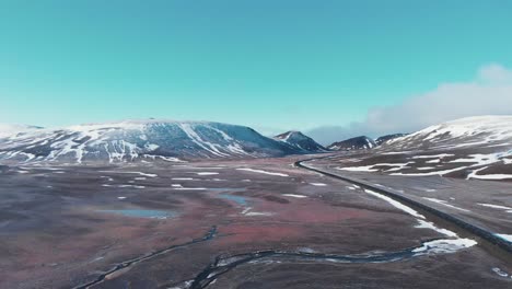 Cars-driving-on-a-highway-in-a-snowy-mountain-valley-in-Iceland,-drone