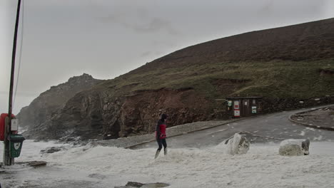 Woman-On-Snow-covered-Chapel-Porth-Beach-As-Winter-Storm-Eunice-Hits-Cornwall-Coast-In-UK