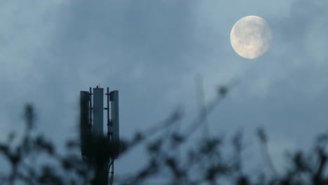 Cloud-passing-moon-behind-cellular-telecommunication-transmitter-tower