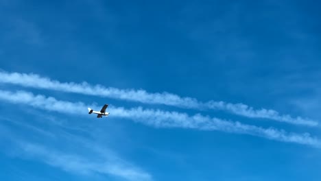 Low-angle-view-of-small-propeller-airplane-in-blue-sky-with-chemtrails