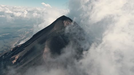 Volcano-peak-surrounded-by-dense-cloudscape-in-Guatemala,-aerial-FPV-view