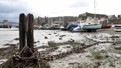 Rotten-derelict-old-pier-wood-debris-and-rusting-chains-on-Conwy-castle-harbour-shoreline
