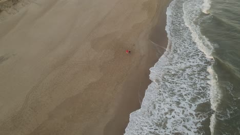Wunderschöne-Drohnenaufnahme-Eines-Paares-Mit-Hund,-Das-Bei-Sonnenuntergang-Am-Strand-Von-Playa-La-Viuda-In-Uruguay-Spazieren-Geht