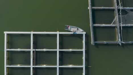 Local-fisherman-docking-boat-on-square-floating-fish-farm-frame,-top-down