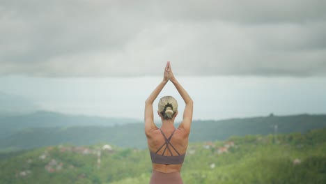 Behind-athletic-woman-raising-hands-into-meditating-namaste-salute,-rural-Bali-background-view