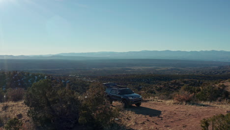 Low-aerial-passing-overland-4x4-SUV-at-scenic-overlook-campsite-in-desert,-4K
