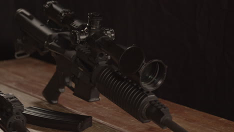 Close-dolly-of-AR-15-rifle-with-scope-standing-on-wooden-table