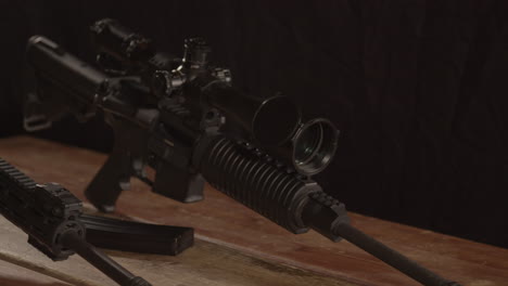Dolly-out-of-AR-15-rifle-with-scope,-revealing-barrel-of-other-rifle-on-wooden-table