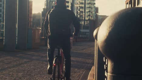 Man-riding-bicycle-in-the-morning,-back-view,-city-background,-filmic-look