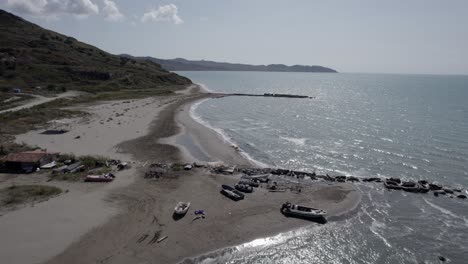 Frontal-drone-video-over-Karpen-beach-in-Albania,-over-flying-wooden-boats,-a-beach-bar,-people-walking-along-the-beach,-dikes-and-the-clear-horizon-in-the-background