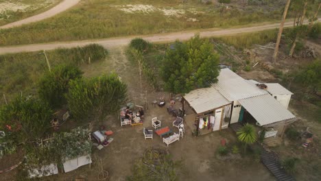 Aerial-circling-over-people-relaxing-in-prefabricated-house-garden-at-sunset,-Punta-del-Diablo-in-Uruguay