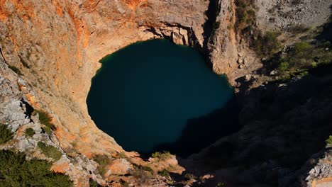 A-drone-shot-of-Red-Lake-or-Crveno-jezero-which-is-a-collapsed-sinkhole-containing-a-karst-lake-close-to-Imotski,-Croatia