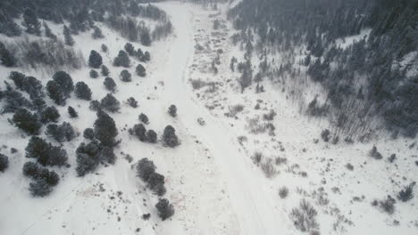 Drone-Aerial-View-of-Land-Rover-Defender-D90-SUV-Parked-on-Snow-Covered-Road-in-Backcountry-Alpine-Forest-Road-in-Rocky-Mountains-near-Nederland-Boulder-Colorado-USA-During-Heavy-Snowfall