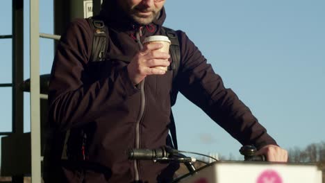A-young-man-on-a-shared-bike-enjoys-a-cup-of-coffee-on-a-sun-kissed-morning
