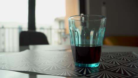 Panning-shot-of-glass-filled-with-cola-standing-on-table-in-kitchen-during-daytime
