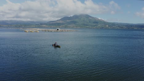 Local-fisherman-checking-his-nets-for-fish-with-fish-farms-floating-in-background,-lake-Batur,-aerial
