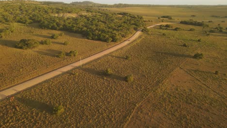 Isolated-car-driving-on-deserted-road-in-rural-landscape-at-sunset,-Punta-del-Diablo-in-Uruguay