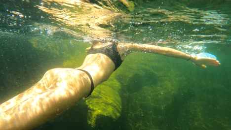Slow-motion-pov-of-woman-swimming-underwater-in-rocky-river-during-sunny-day-,4k-following-shot