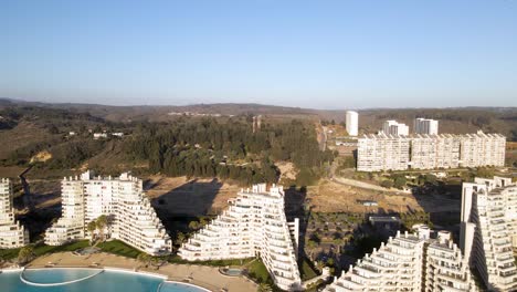 Aerial-dolly-back-over-obuildings-with-a-huge-pool-next-to-the-beach-at-Algarrobo,-Chile
