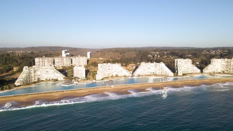 Aerial-orbit-over-a-huge-swimming-pool-next-to-modern-buildings-at-beach-of-Algarrobo,-Chile