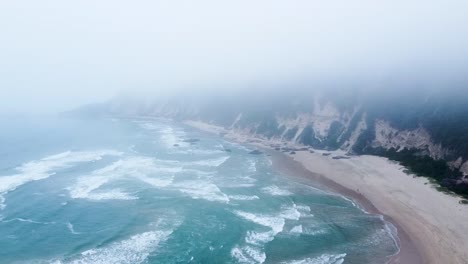 An-aerial-drone-shot-flying-below-a-blanket-of-clouds-as-a-low-pressure-system-brings-winter-rainfall-and-choppy-surf-in-Sedgefield,-Western-Cape,-South-Africa