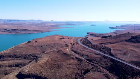 Aerial-Drone-shot-pan-to-reveal-the-vast-spanning-beautiful-blue-waters-of-the-Driefkloof-Dam,-the-reservoir-surrounded-by-a-dry-dusty-lifeless-landscape,-Free-State,-South-Africa