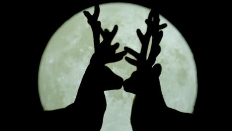 Silhouetted-miniature-reindeer-couple-kissing-against-white-moonlight-backdrop