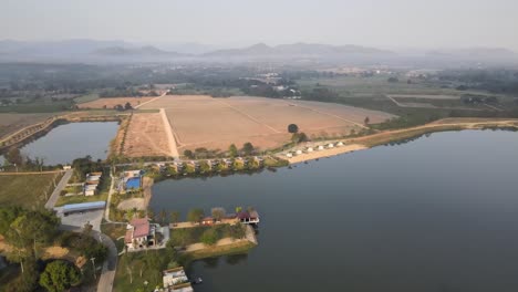 Aerial-Orbital-Drone-Shot-of-a-Lake-and-Hotel-Resort-with-Scenic-Landscape-in-the-Background-in-Thailand