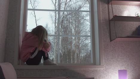 Blonde-little-girl-curled-up-at-the-window-swinging-looking-out