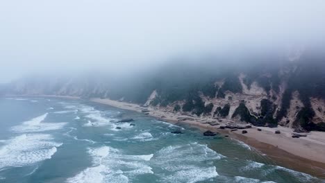 Aerial-drone-shot-of-a-misty-ocean-shoreline-in-Sedgefield,-a-popular-travel-destination-along-the-Garden-Route-in-the-Western-Cape,-South-Africa