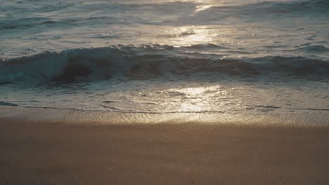 Kleine-Wellen-Des-Pazifischen-Ozeans-Rollen-Auf-Einen-Wunderschönen-Braunen-Sandstrand,-Während-Die-Untergehende-Sonne-Auf-Dem-Wasser-Versinkt