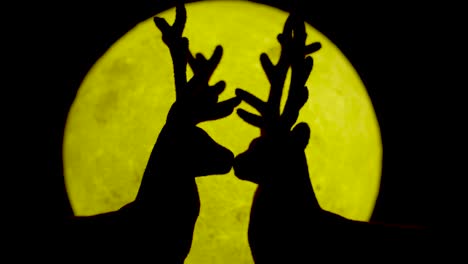 Miniature-reindeer-couple-kissing-against-yellow-moonlight-backdrop
