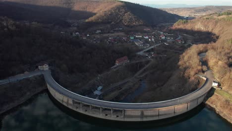 Aerial-reveal-of-the-dam-holding-back-the-water-reservoir-from-the-small-town-in-the-valley