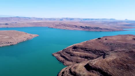 Aerial-Drone-shot-panning-around-to-reveal-the-beautiful-blue-water-of-the-Driefkloof-Dam,-the-dam-surrounded-by-dry-burnt-veld,-Free-State,-South-Africa