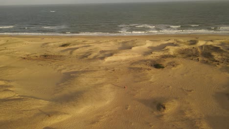 People-walking-on-sand-dunes-by-beach,-rotating-aerial-view