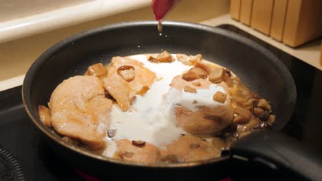Pouring-White-Cream-On-Chicken-With-Mushrooms-On-A-Cooking-Pan---close-up