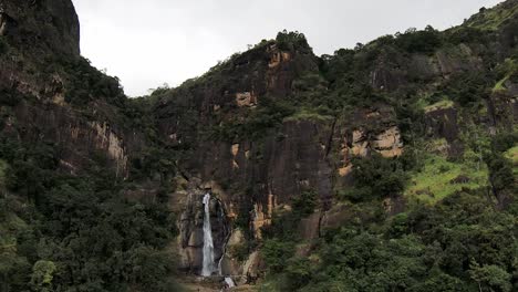 Aerial-Drone-Of-Tall-Rocky-Cliffs-And-Ravana-Falls-Waterfall-With-Green-Trees-In-Ella-Sri-Lanka