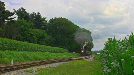 A-Front-View-of-an-Antique-Steam-Passenger-Train-Approaching-Traveling-Thru-Farmlands-and-Corn-Fields-Blowing-Smoke-on-a-Sunny-Summer-Day