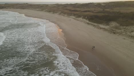 Couple-walking-on-beach-at-sunset,-Playa-La-Viuda