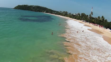 Luftdrohne-über-Touristen,-Die-Am-Beliebten-Strand-Mit-Türkisfarbenem-Wasser-Im-Tropischen-Sri-Lanka-Schwimmen