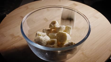 Gehackte-Reife-Bananen,-Die-In-Eine-Glasschüssel-Auf-Den-Tisch-Fallen