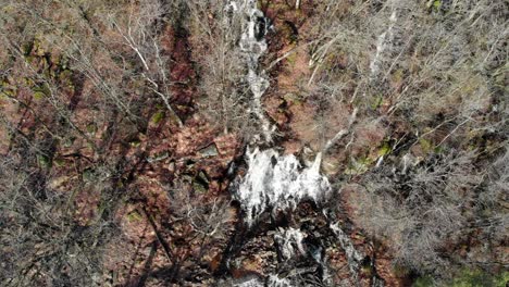 Aerial-View-Of-Gushing-Waterfall-Through-The-Forest-At-Late-Winter