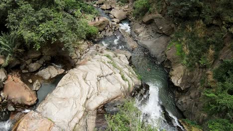 Slow-Motion-Shot-Of-Deep-Rocky-Waterfall,-Tourists-Enjoying-Water-Breeze-Down-Valley,-Sri-Lanka