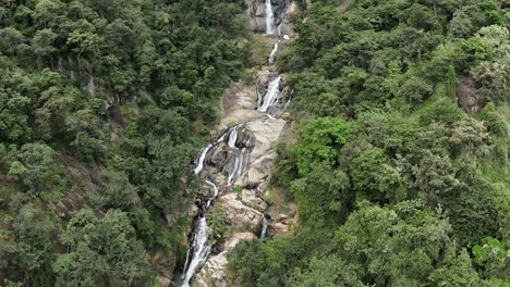 Tiro-Inclinado-Hacia-Arriba-De-Una-Hermosa-Cascada-Que-Fluye-Hacia-Abajo-En-Un-Amplio-Valle-Verde,-Sri-Lanka