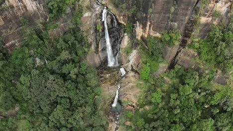 Luftaufnahme-In-Zeitlupe-Eines-Atemberaubenden-Wasserfalls,-Der-Aus-Einem-Felsigen-Bergloch-Strömt,-Sri-Lanka